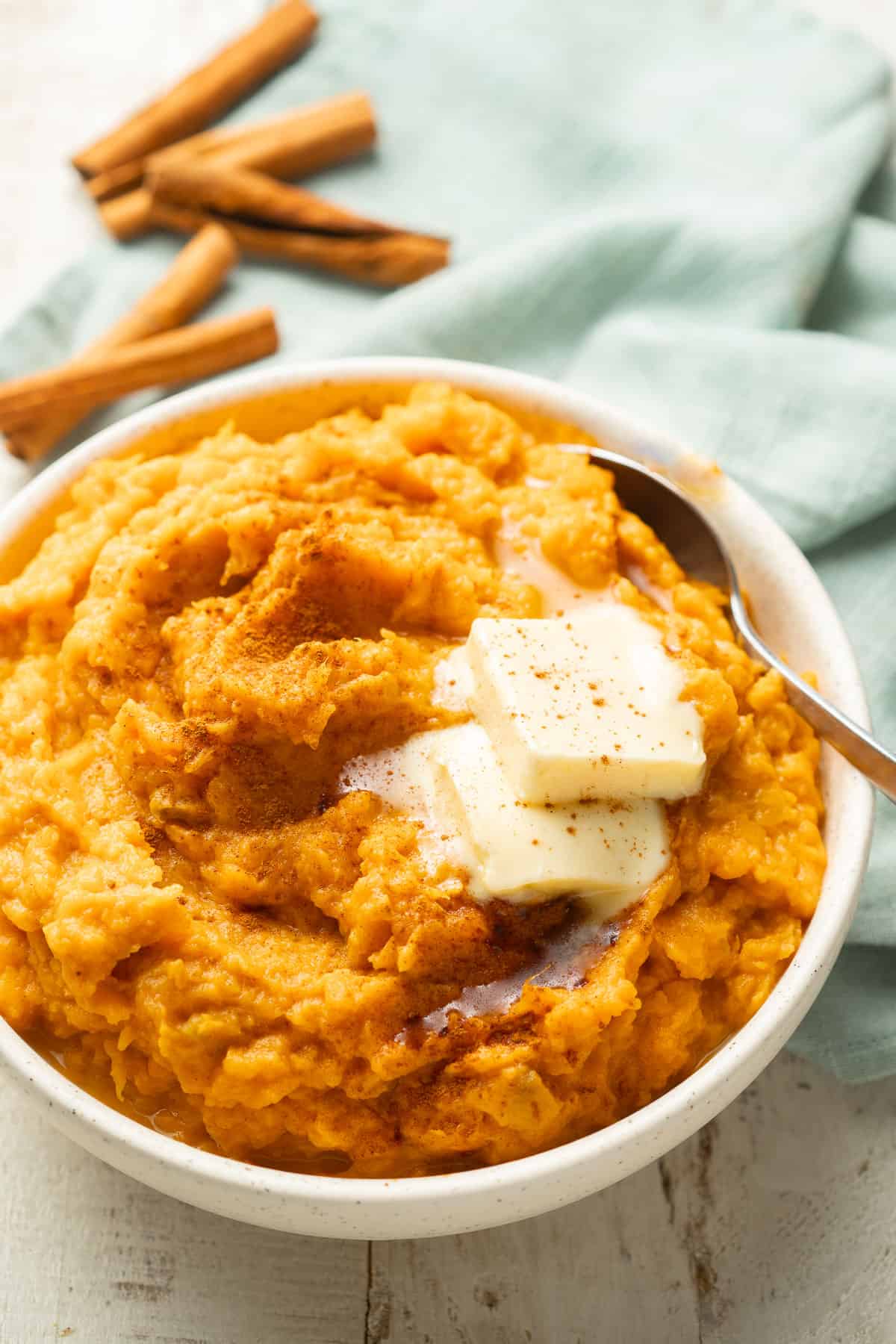Bowl of Vegan Mashed Sweet Potatoes with cinnamon sticks in the background.