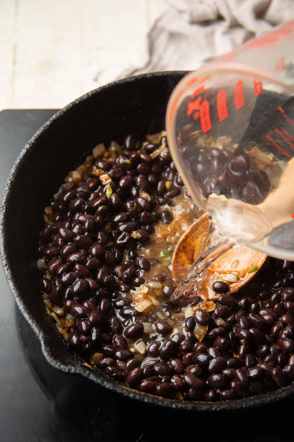 Water being poured into a skillet of black beans.