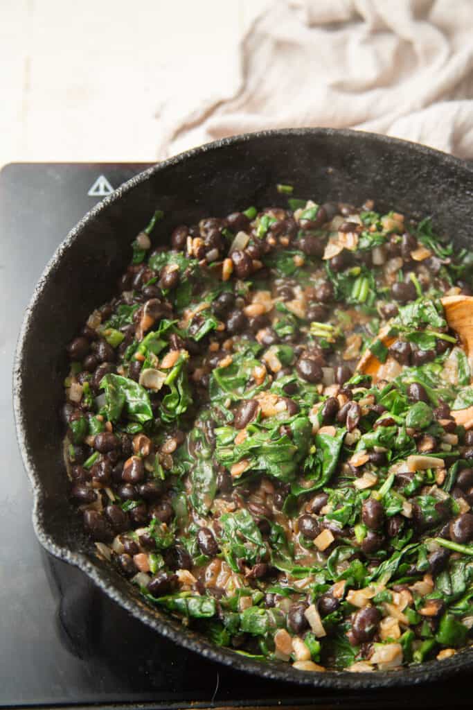 Skillet of black beans and spinach on a cook top.