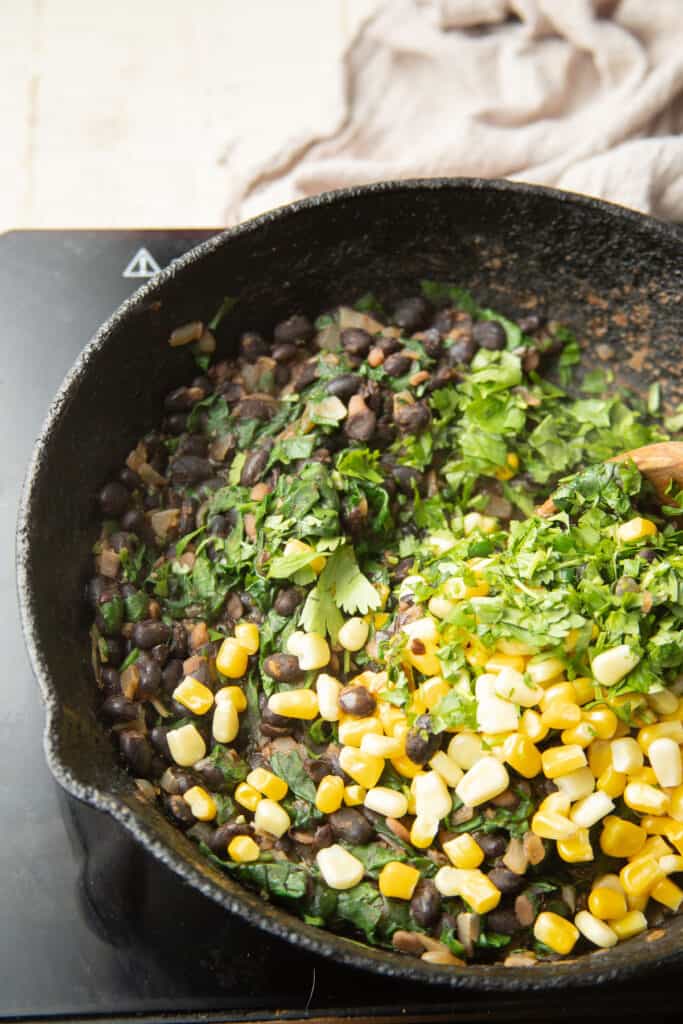 Skillet of black beans with corn and chopped cilantro on top.
