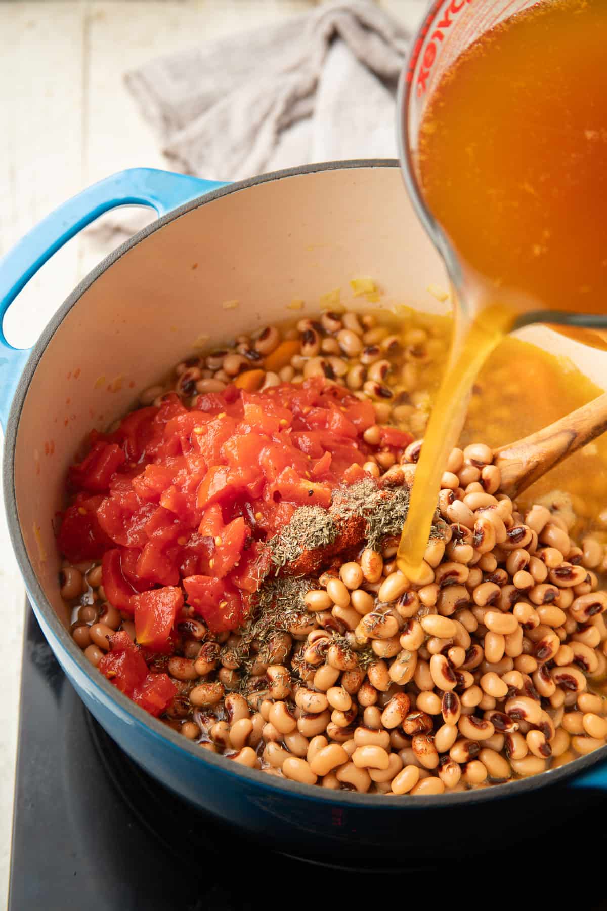 Broth being poured into a pot of black-eyed peas, tomatoes and spices.