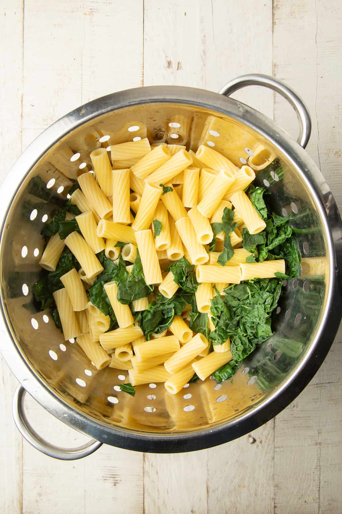Blanched kale and cooked rigatoni pasta in a colander.