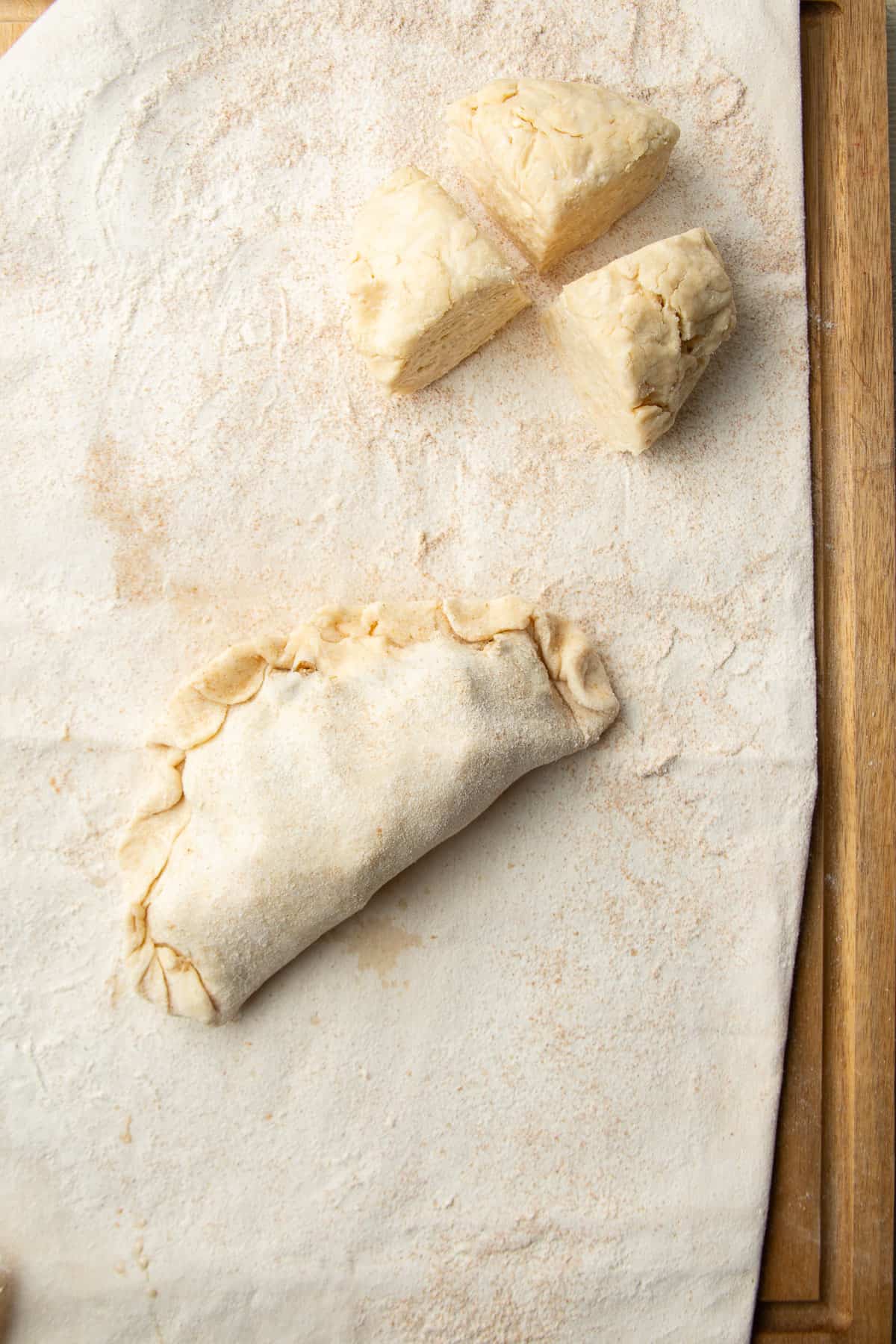 Three chunks of dough and one unbaked Vegan Cornish Pasty on a pastry cloth.