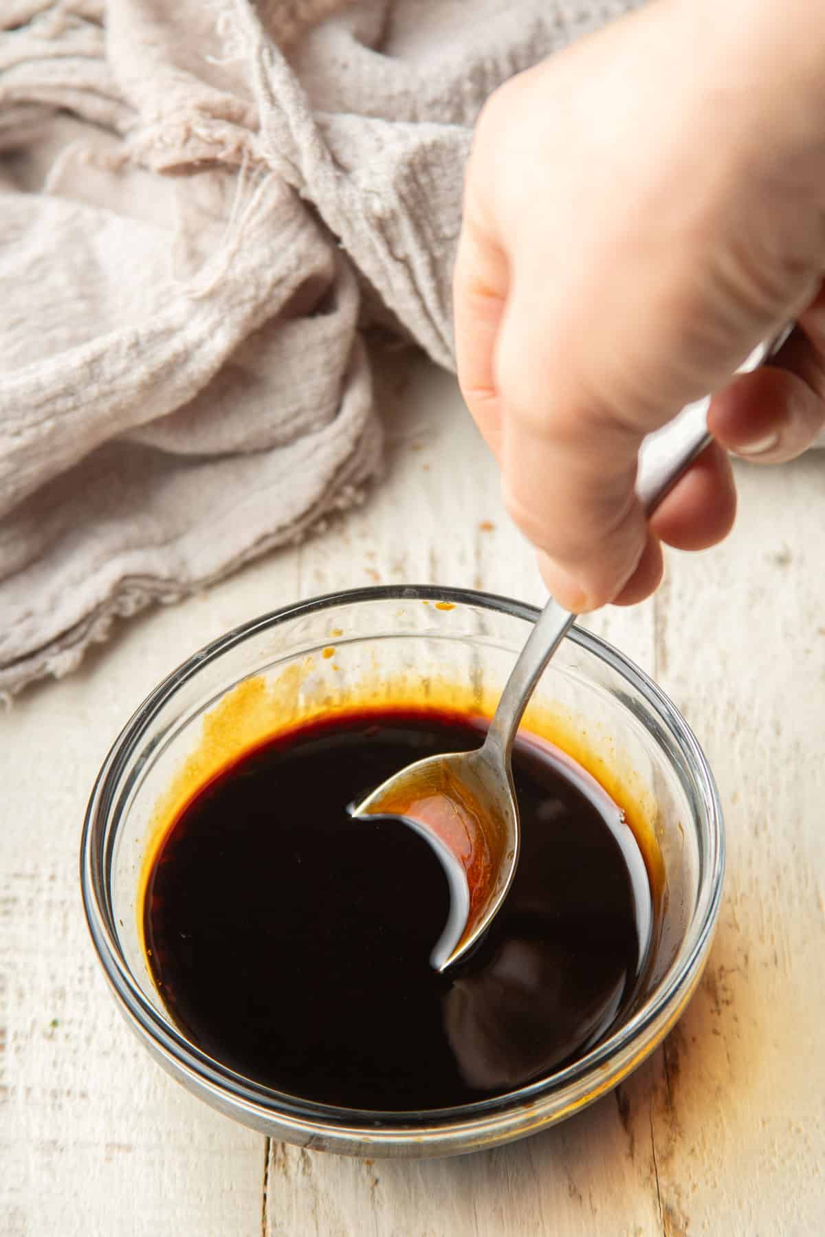 Hand stirring sauce in a small glass bowl.