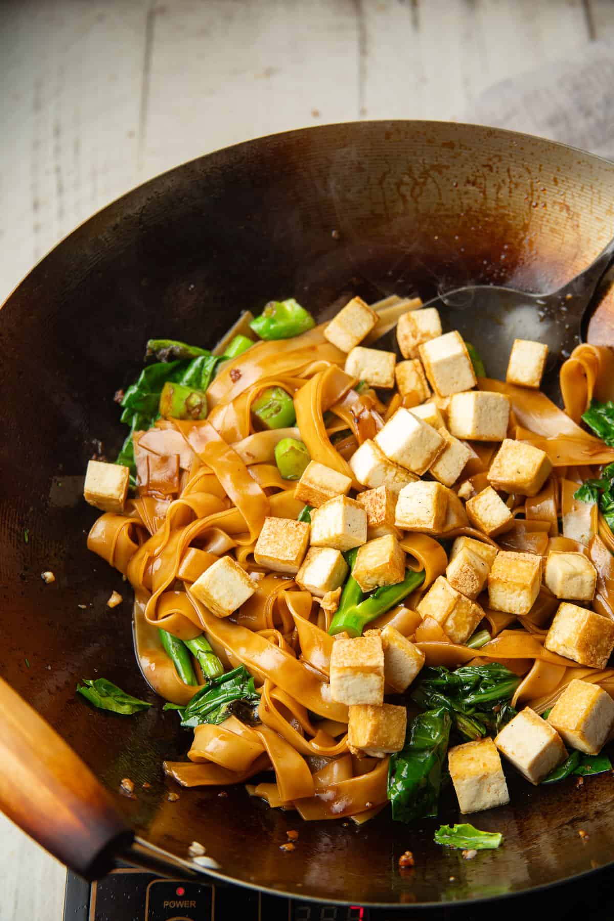 Vegan Pad See Ew in a wok with pan-fried tofu cubes on top.