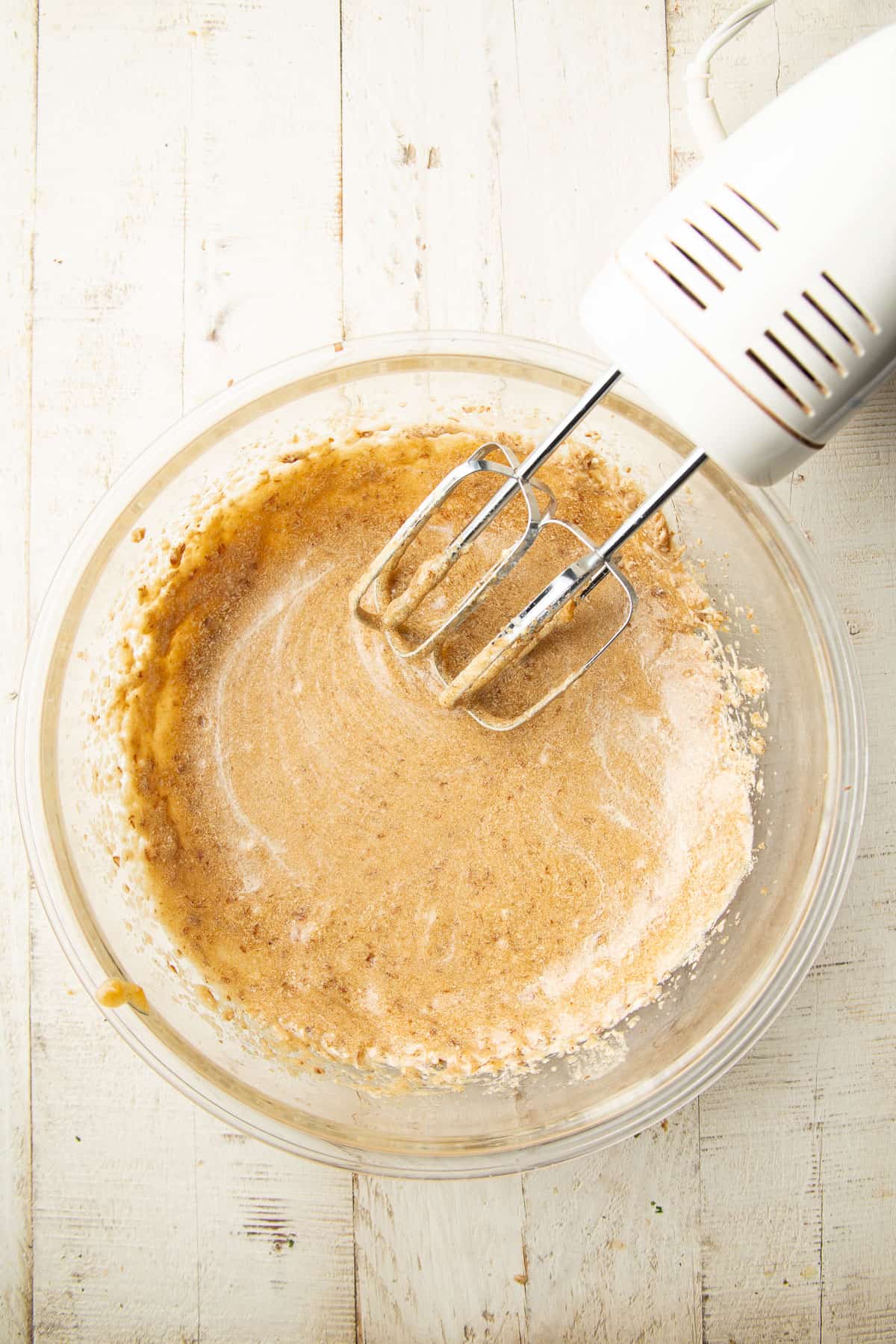 Blended vegan butter, brown sugar, flax egg, and date puree in a mixing bowl with electric mixer.