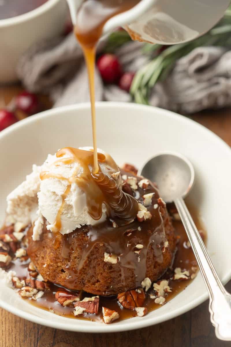 Toffee sauce being drizzled over Vegan Sticky Toffee Pudding and ice cream in a bowl.