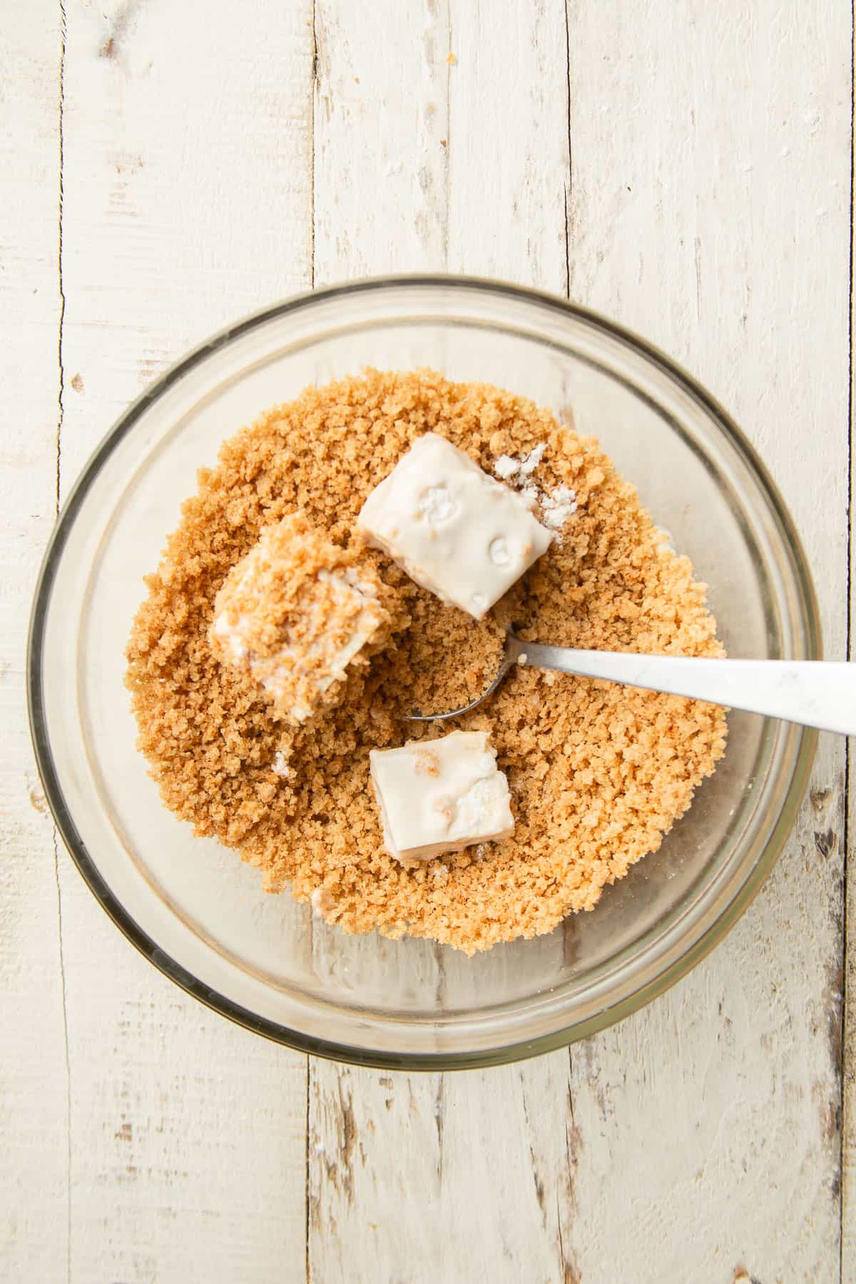 Three tofu cubes in a bowl of panko breadcrumbs with a spoon.