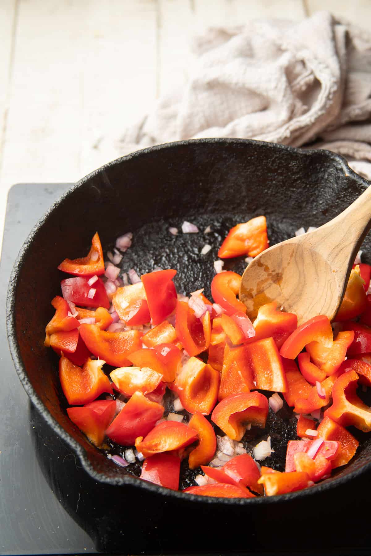 Diced bell pepper and shallots cooking in a cast iron skillet.