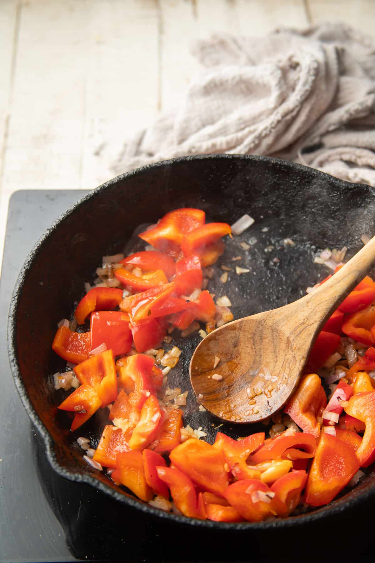 Chopped red peppers, shallots, garlic and balsamic reduction cooking in a skillet with wooden spoon.