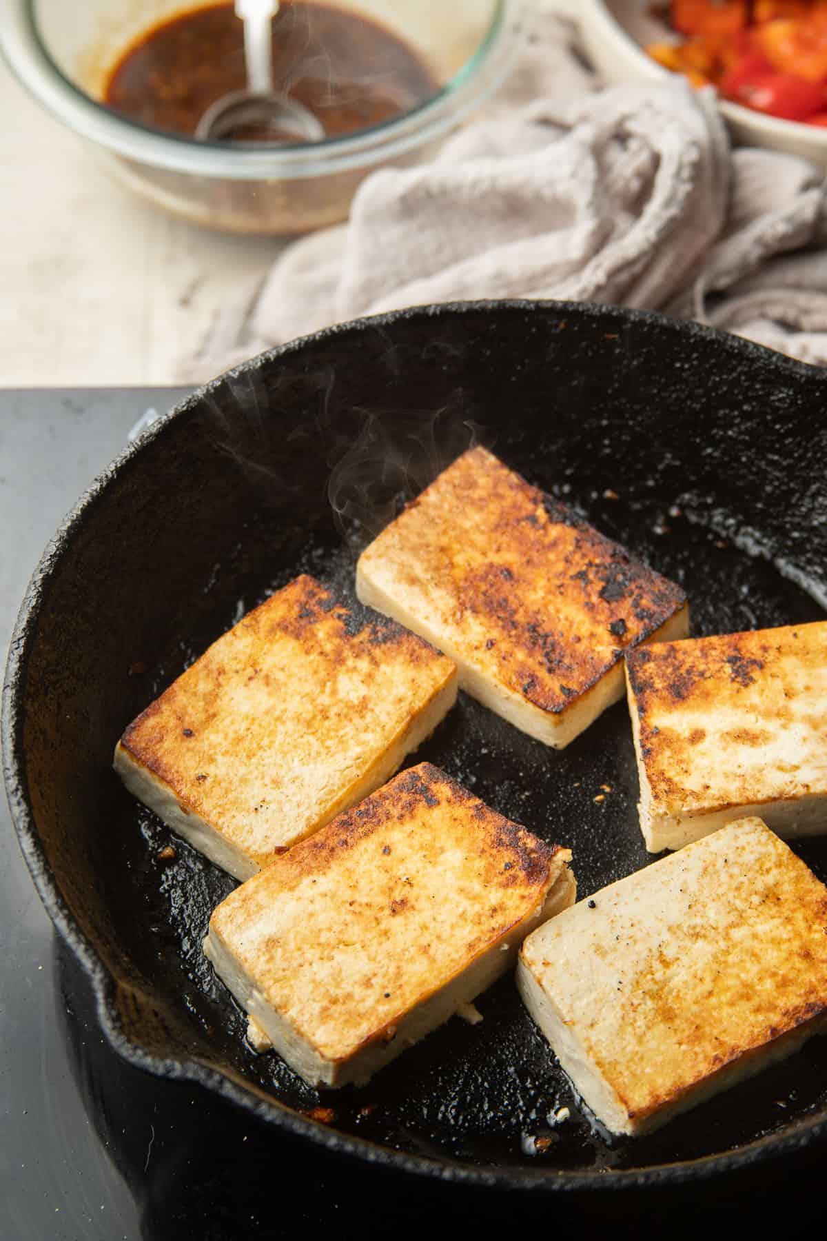 Tofu slabs cooking in a skillet, showing browning on their tops.