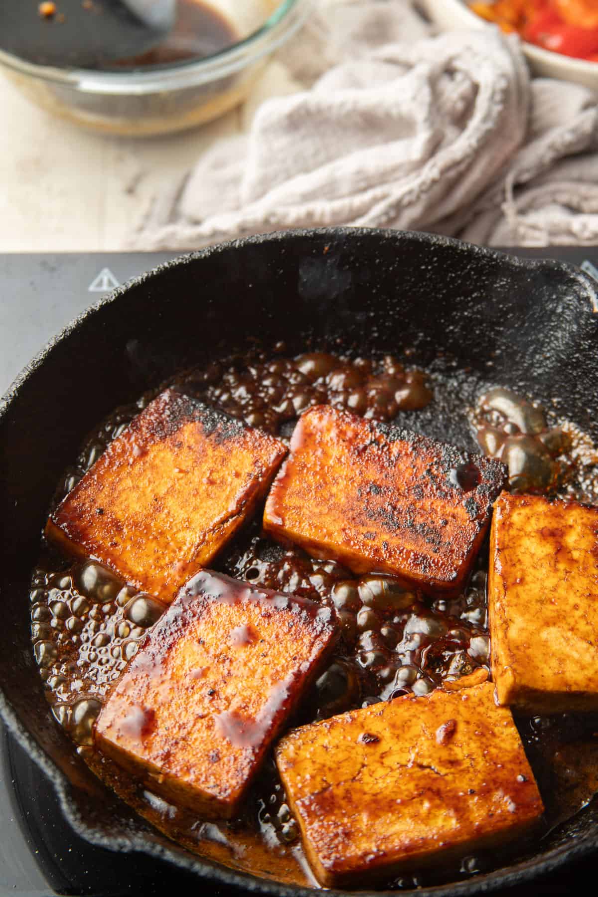 Tofu slabs cooking in a balsamic reduction in a skillet.