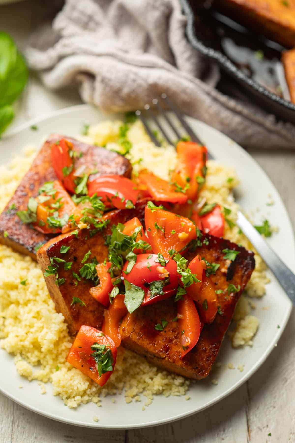 Balsamic Tofu Steaks over couscous on a plate, with a cast iron skillet in the background.
