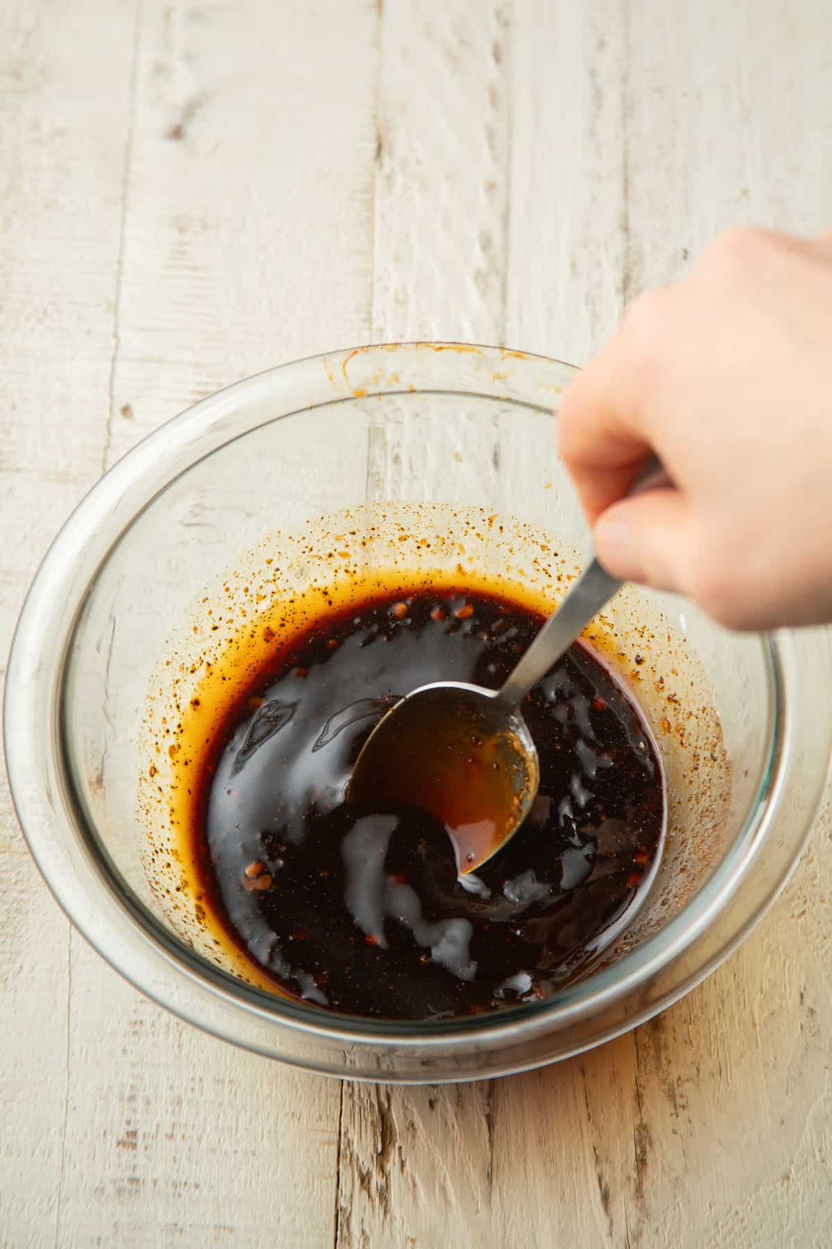 Hand stirring black pepper sauce ingredients together in a glass bowl.