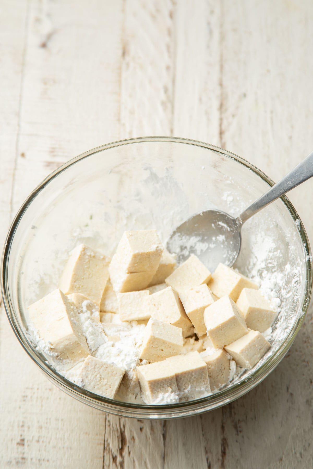 Tofu cubes in a bowl of cornstarch with a spoon.