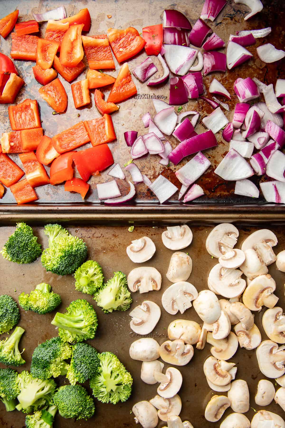 Chopped red pepper, red onion, broccoli, and sliced mushrooms on two baking sheets.