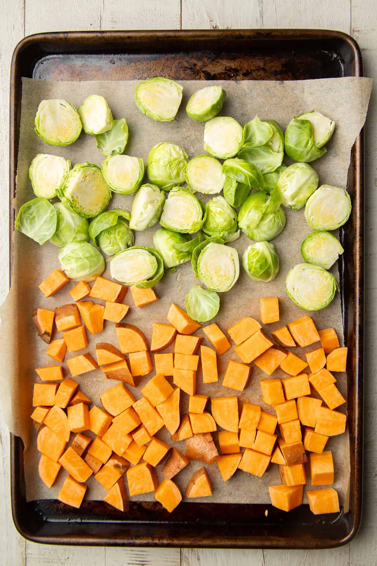 Diced sweet potato and halved Brussels sprouts on a parchment paper-lined baking sheet.