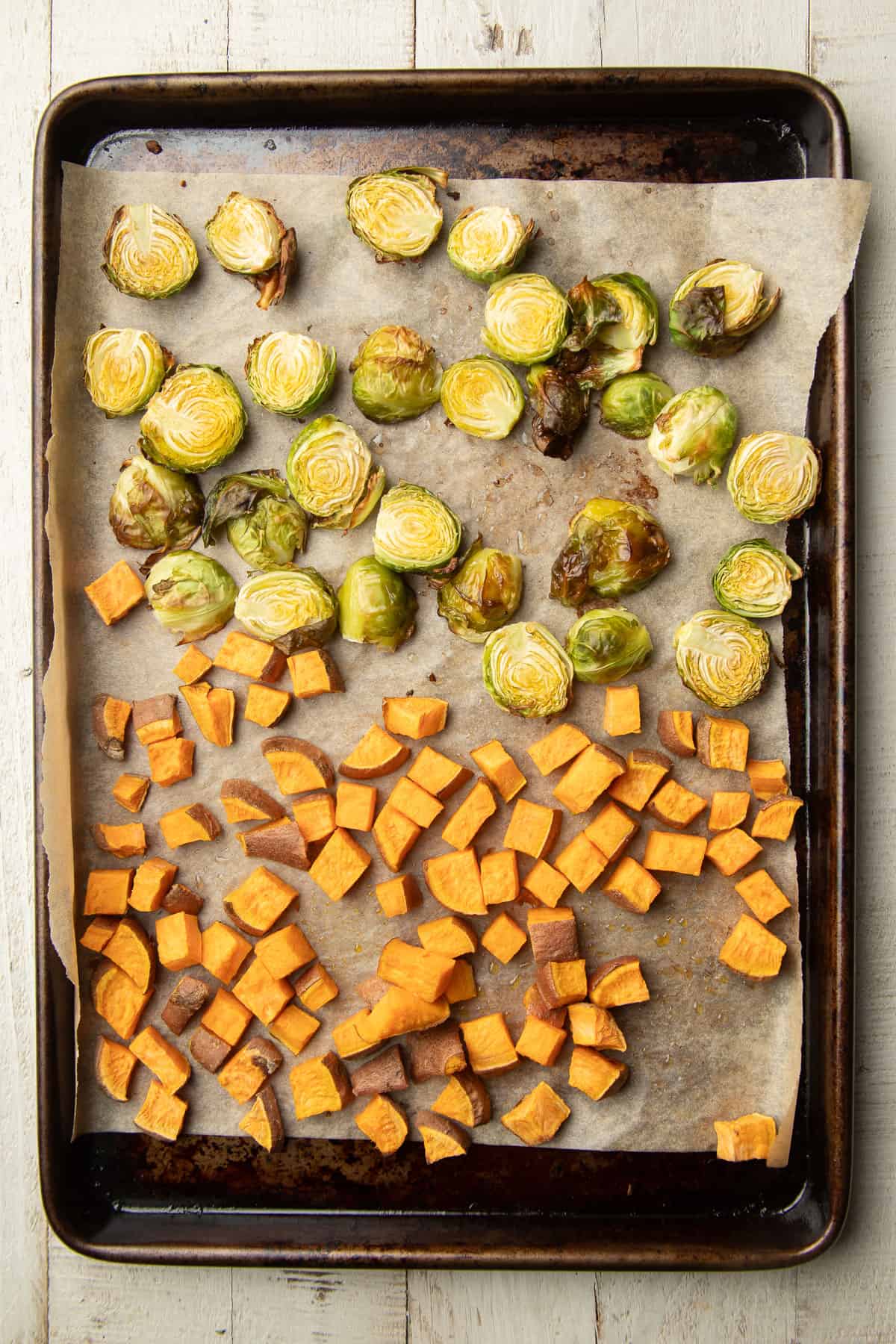 Roasted Brussels sprouts and diced sweet potato on a parchment paper-lined baking sheet.