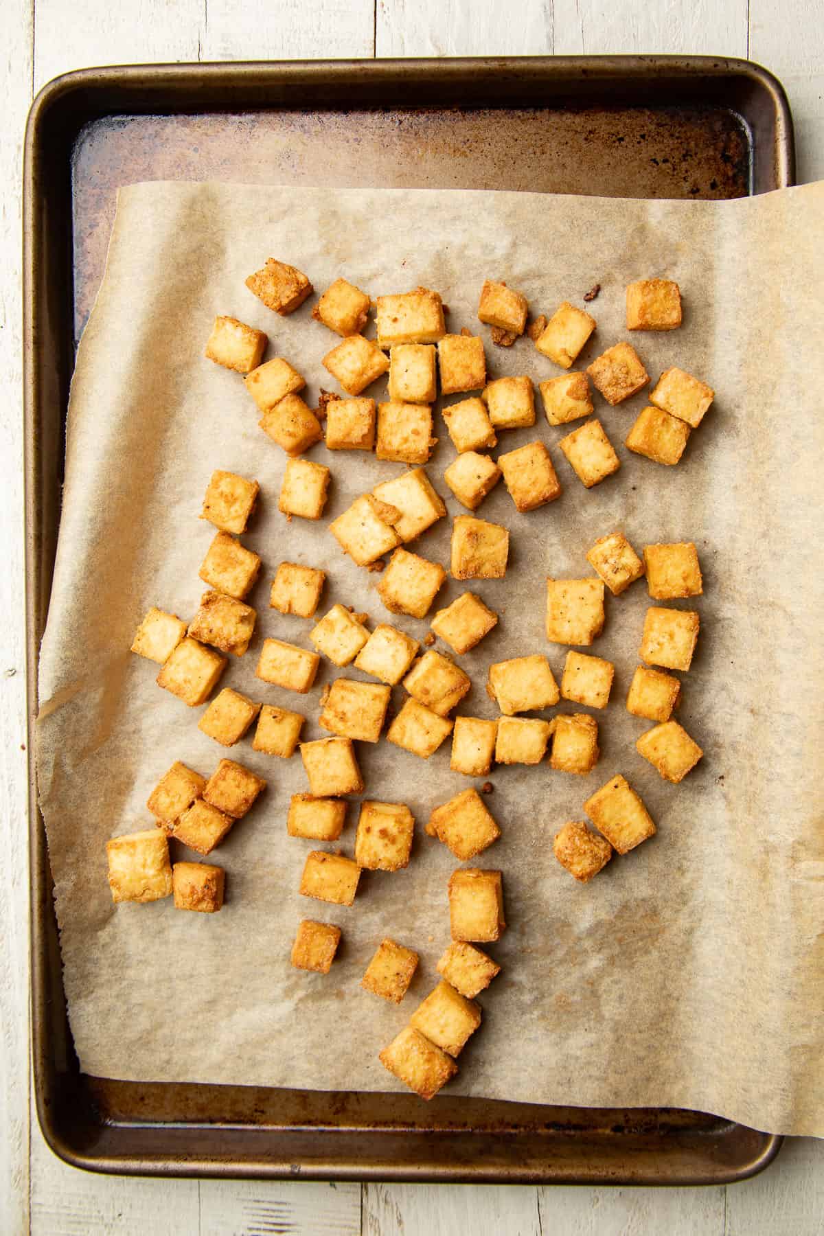 Baked tofu cubes on a parchment paper-lined baking sheet.