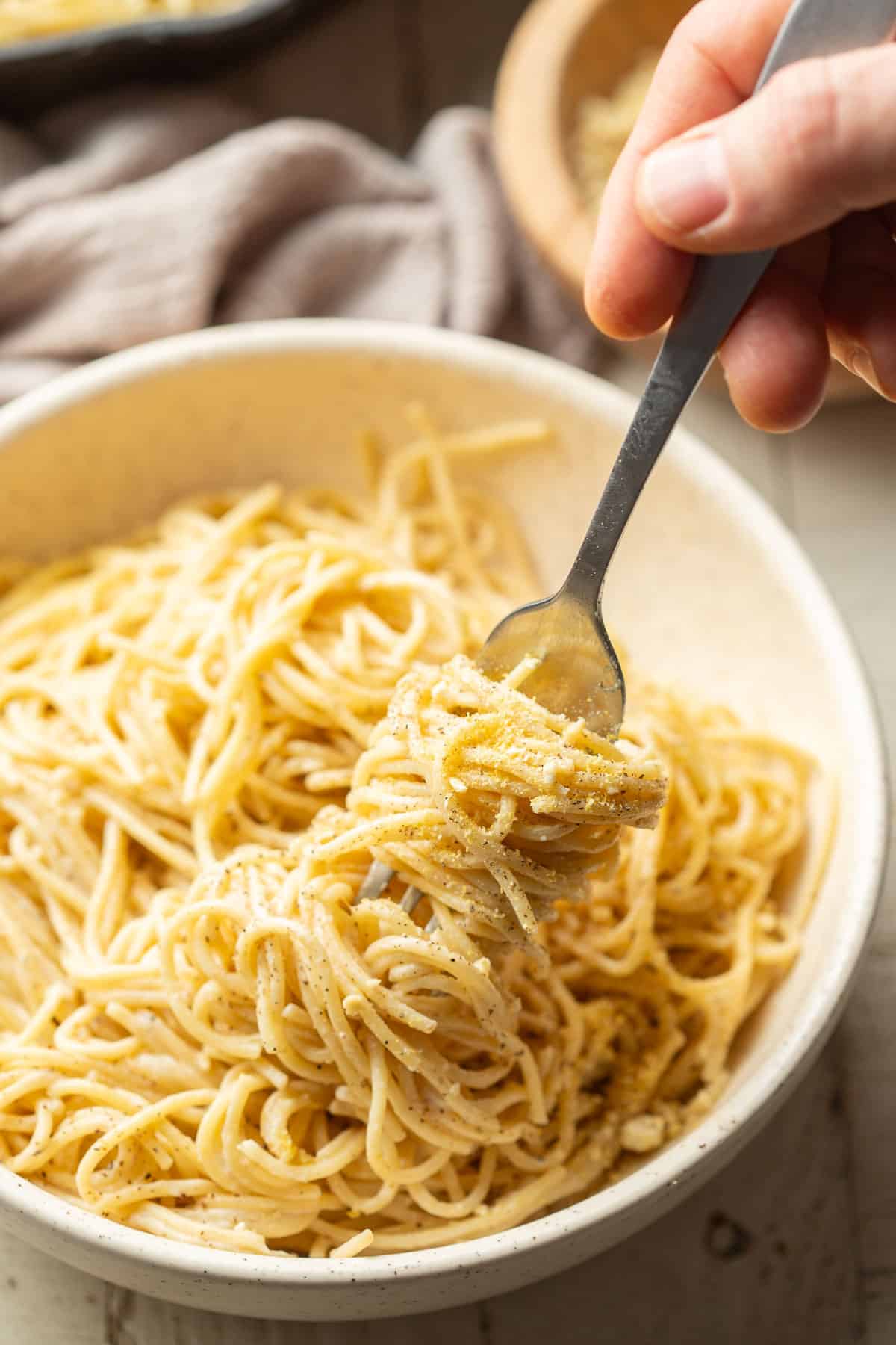 Hand wrapping a cluster of noodles around a fork in a bowl of Vegan Cacio e Pepe.