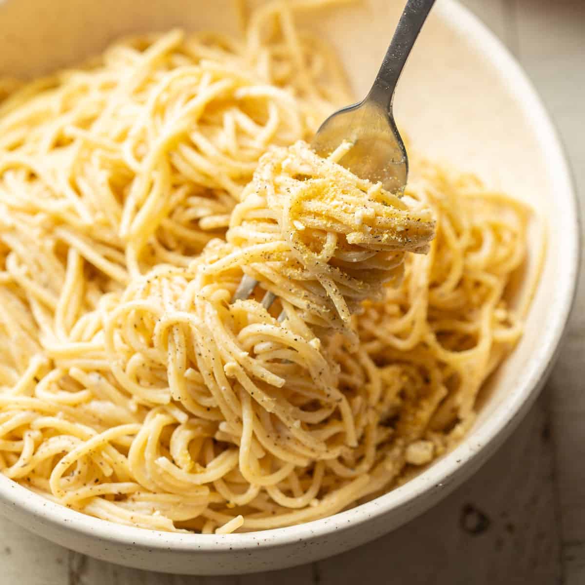 Fork in a bowl of Vegan Cacio e Pepe with a cluster of noodles wrapped around it.