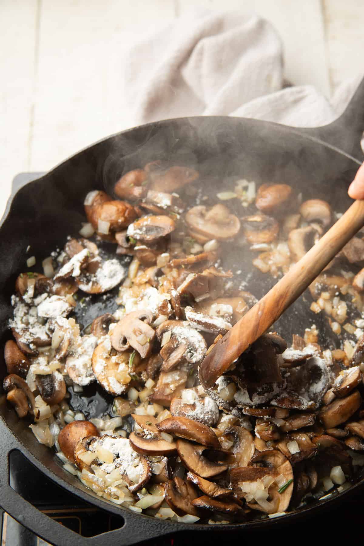 Mushrooms and onions cooking in a skillet with flour sprinkled on top.