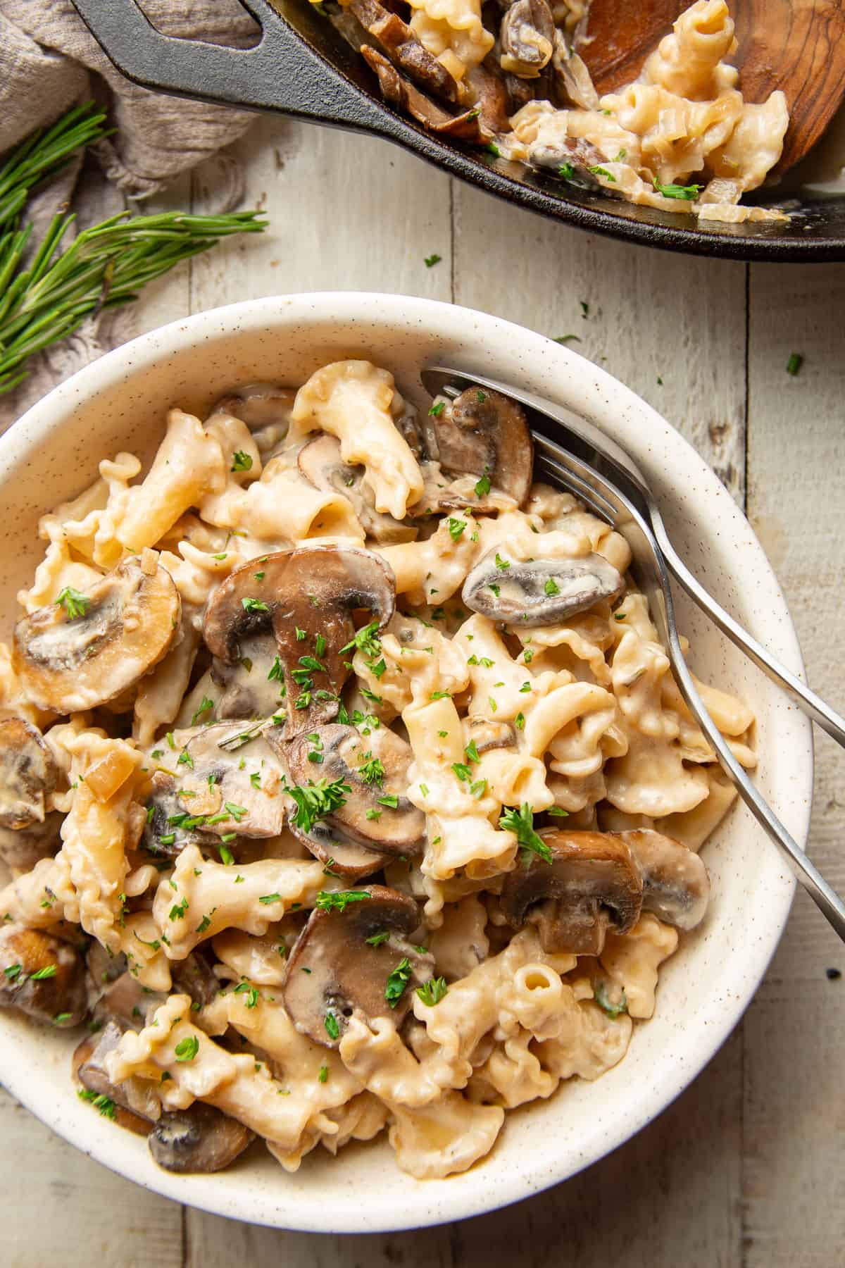 White wooden surface set with skillet and bowl of Vegan Mushroom Stroganoff.