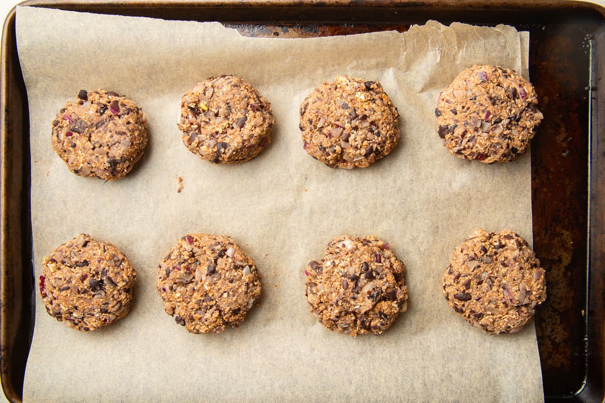 Unbaked black bean slider patties on a parchment paper-lined baking sheet.