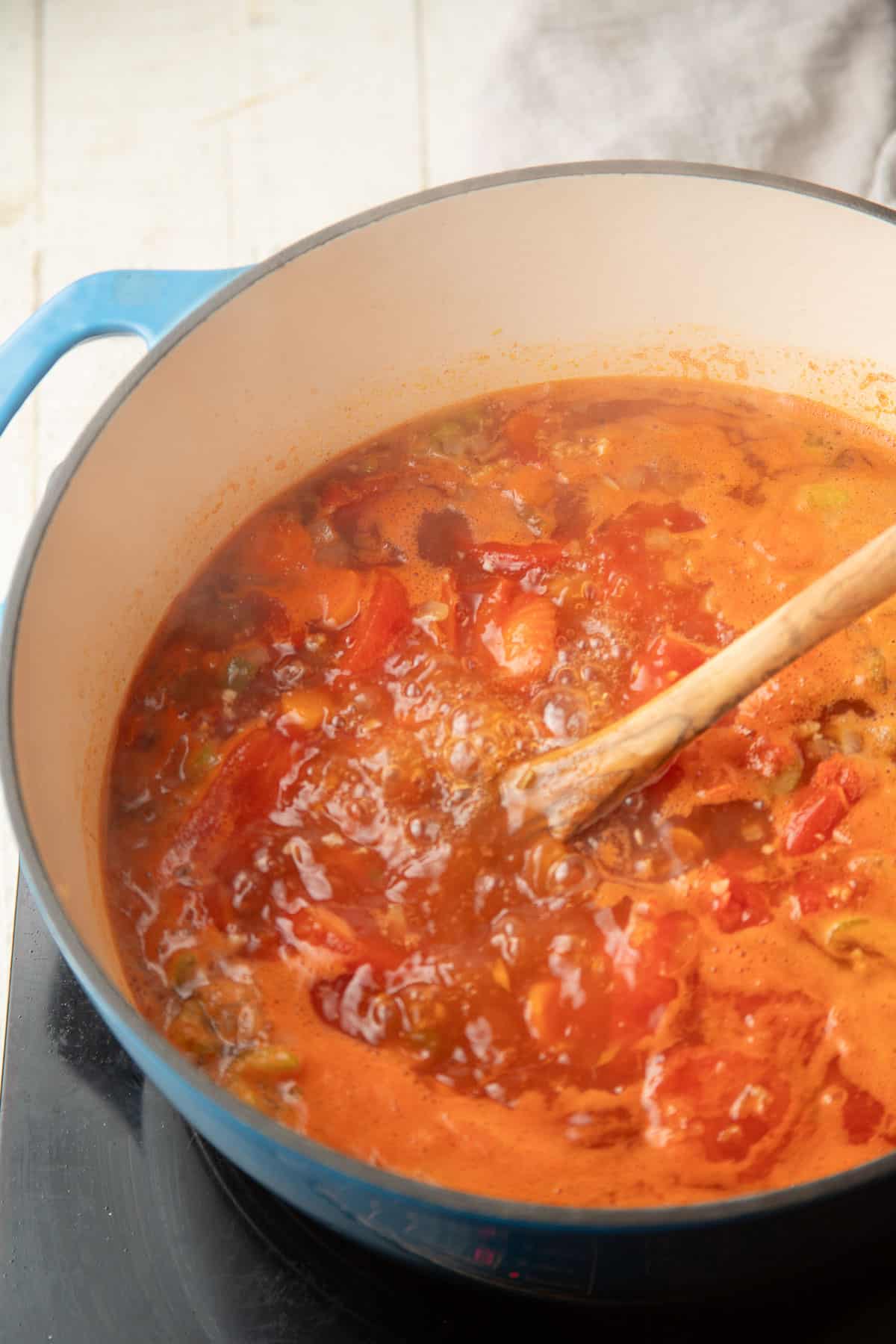 Tomatoes simmering in broth in a blue pot.