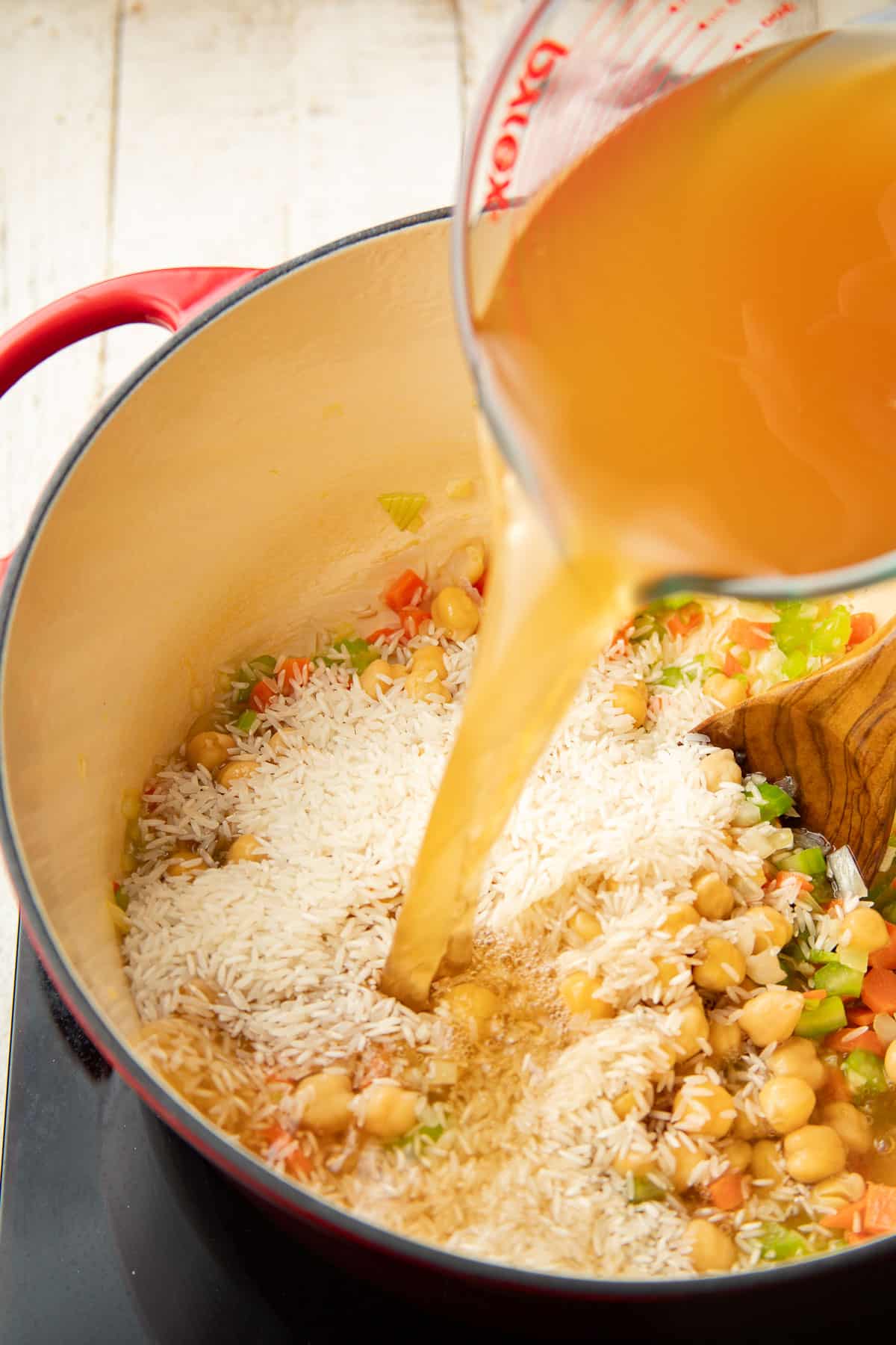 Broth being poured into a pot of chickpeas, rice and vegetables.