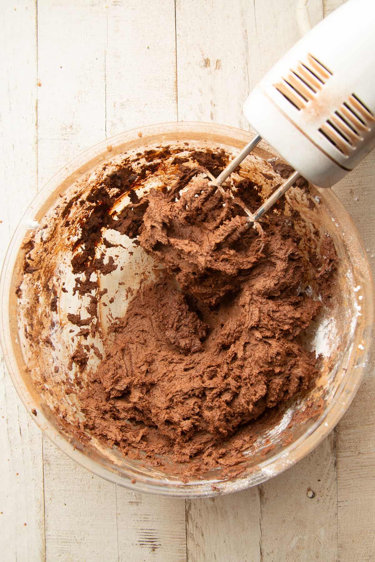 Chocolate cookie dough in a bowl with an electric mixer.