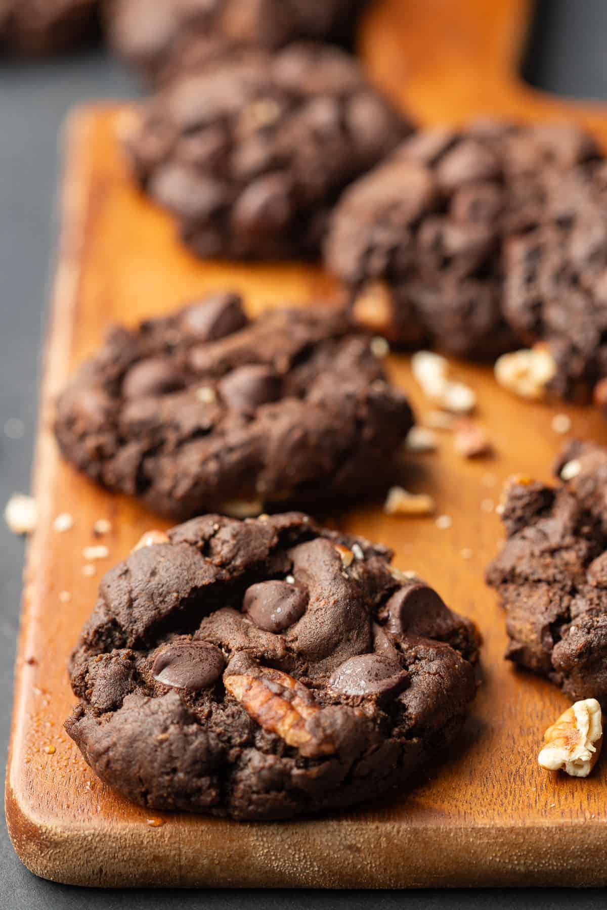 Vegan Double Chocolate Cookies arranged on a wooden cutting board sprinkled with pecan pieces.