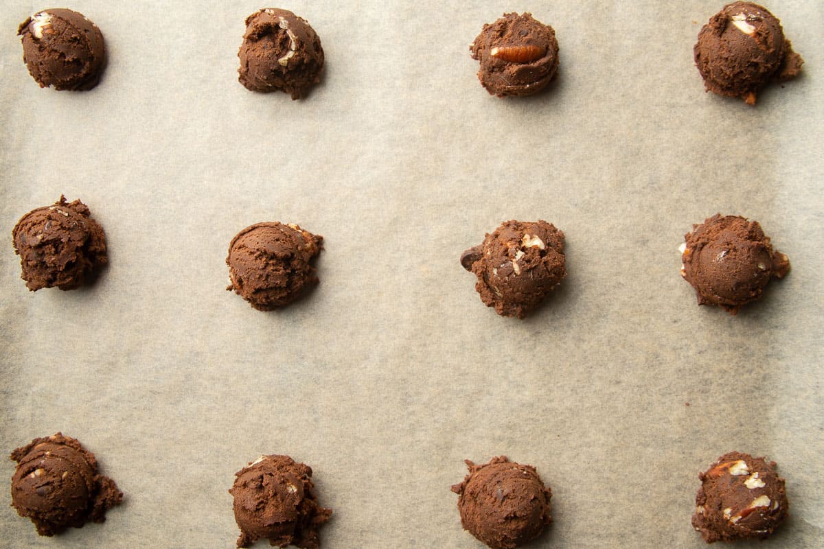 Chocolate dough balls arranged on a parchment paper-lined baking sheet.