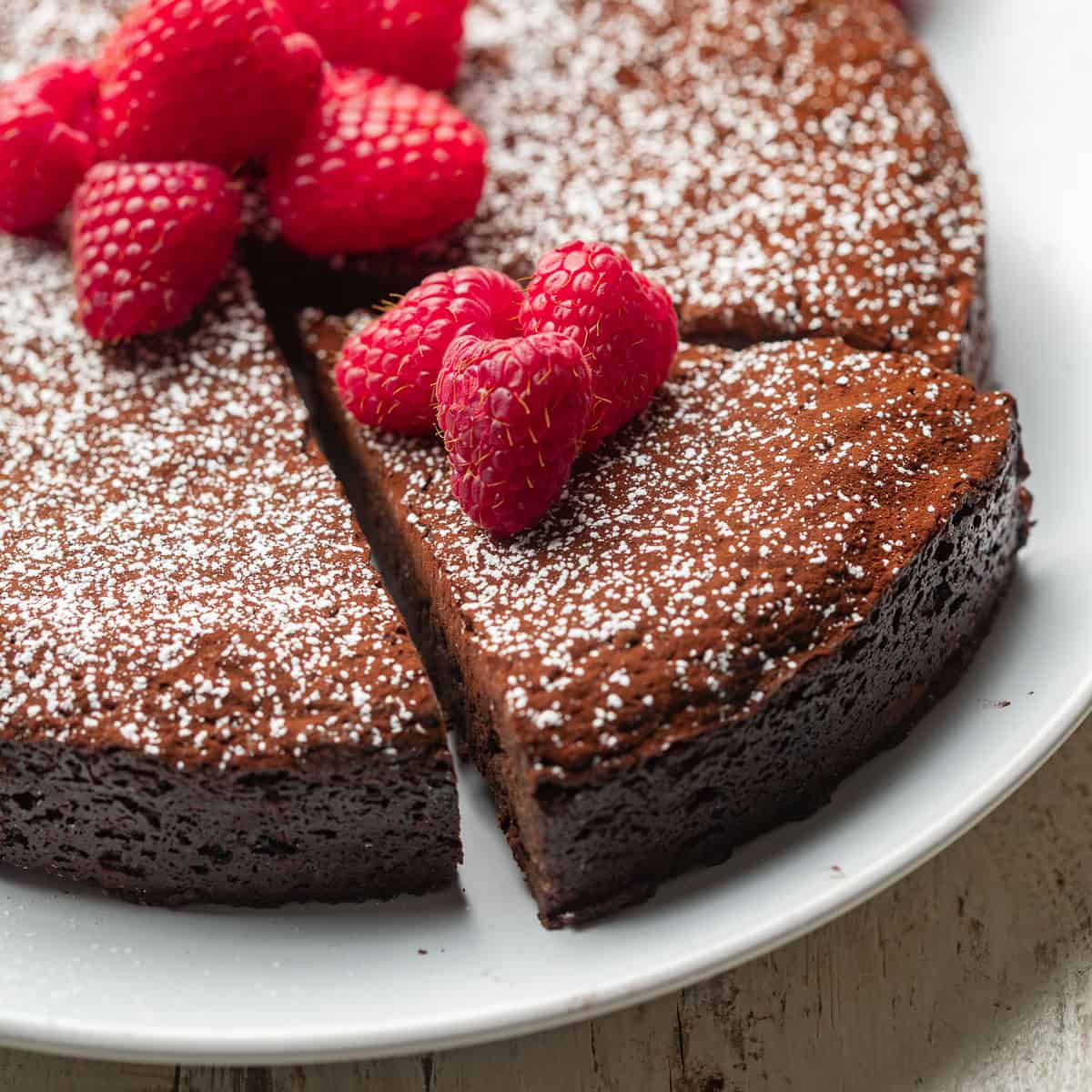 Vegan Chocolate Torte on a plate with a slice cut out and raspberries on top.