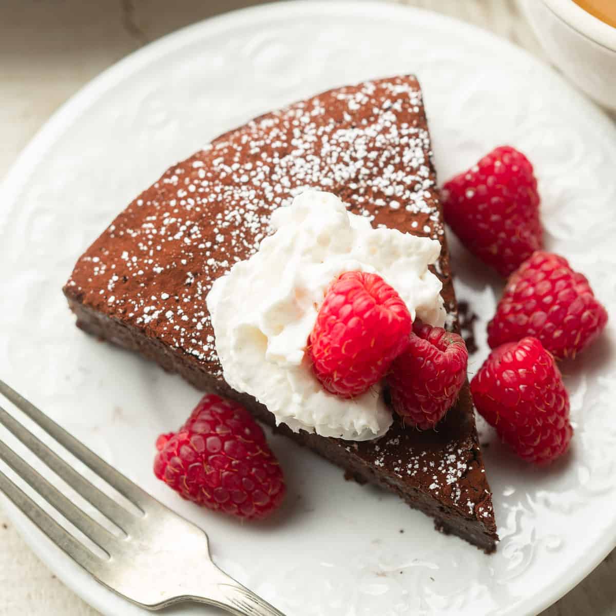 Vegan Chocolate Torte slice on a dish with raspberries and whipped cream.