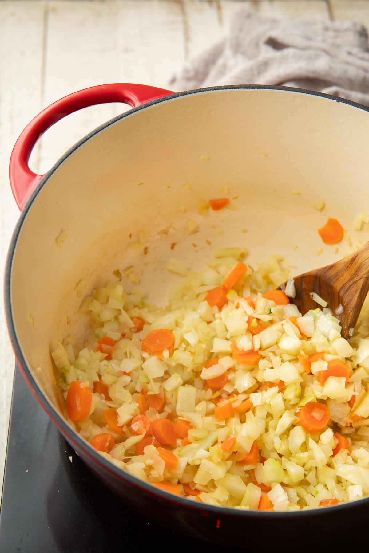 Diced onion, fennel, sliced carrots, and minced garlic cooking in a pot.