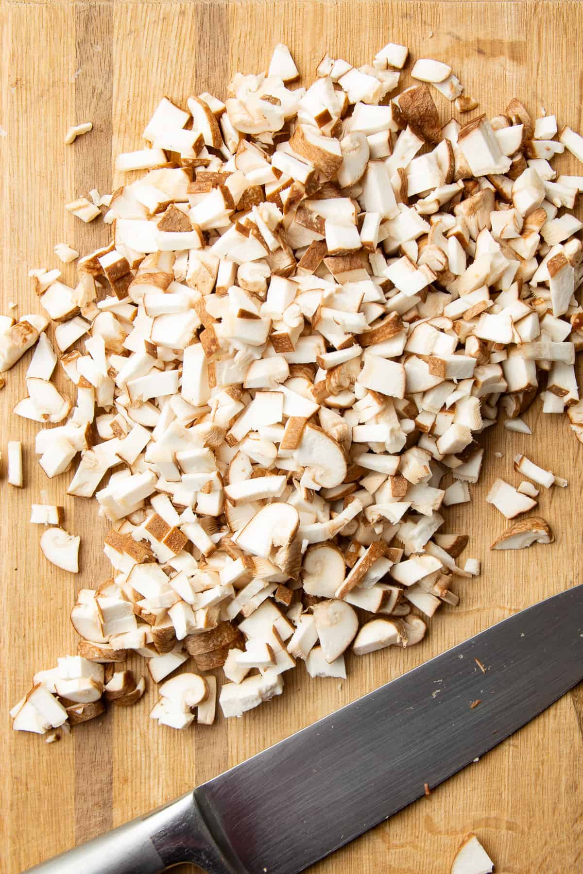 Finely chopped shiitake mushrooms on a cutting board with knife.