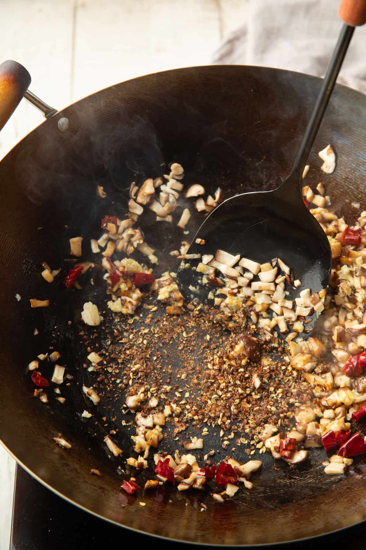 Szechuan peppercorns cooking in a wok wiht dried chiles, shiitake mushrooms, and aromatics.