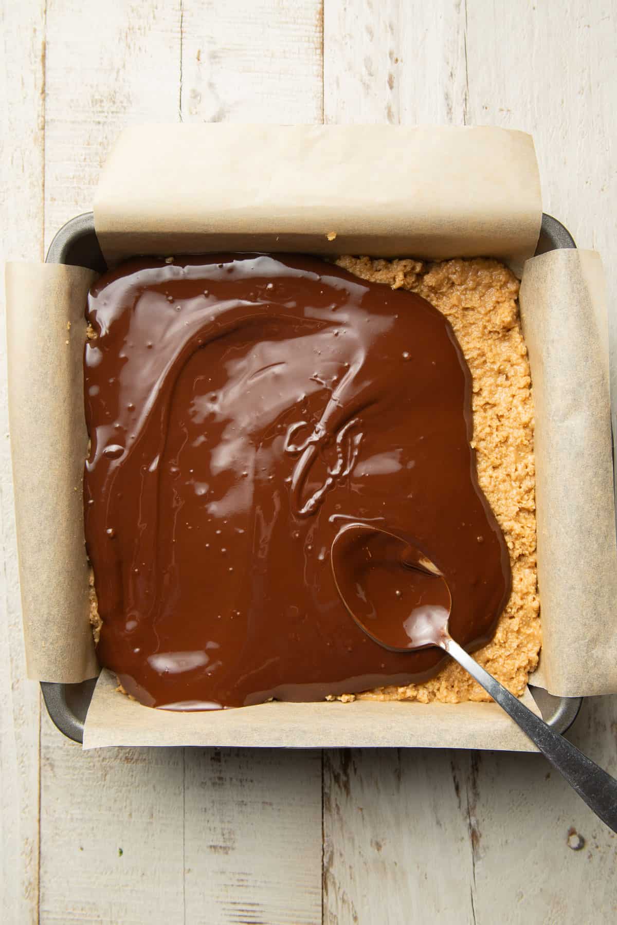 Melted chocolate over a base of peanut butter and graham cracker crumbs in a baking pan.