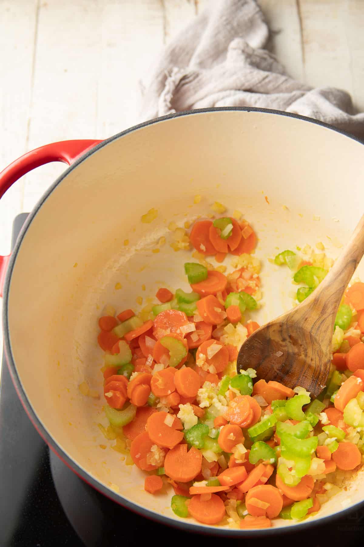 Celery, onions, carrots, and garlic cooking in a pot with a wooden spoon.