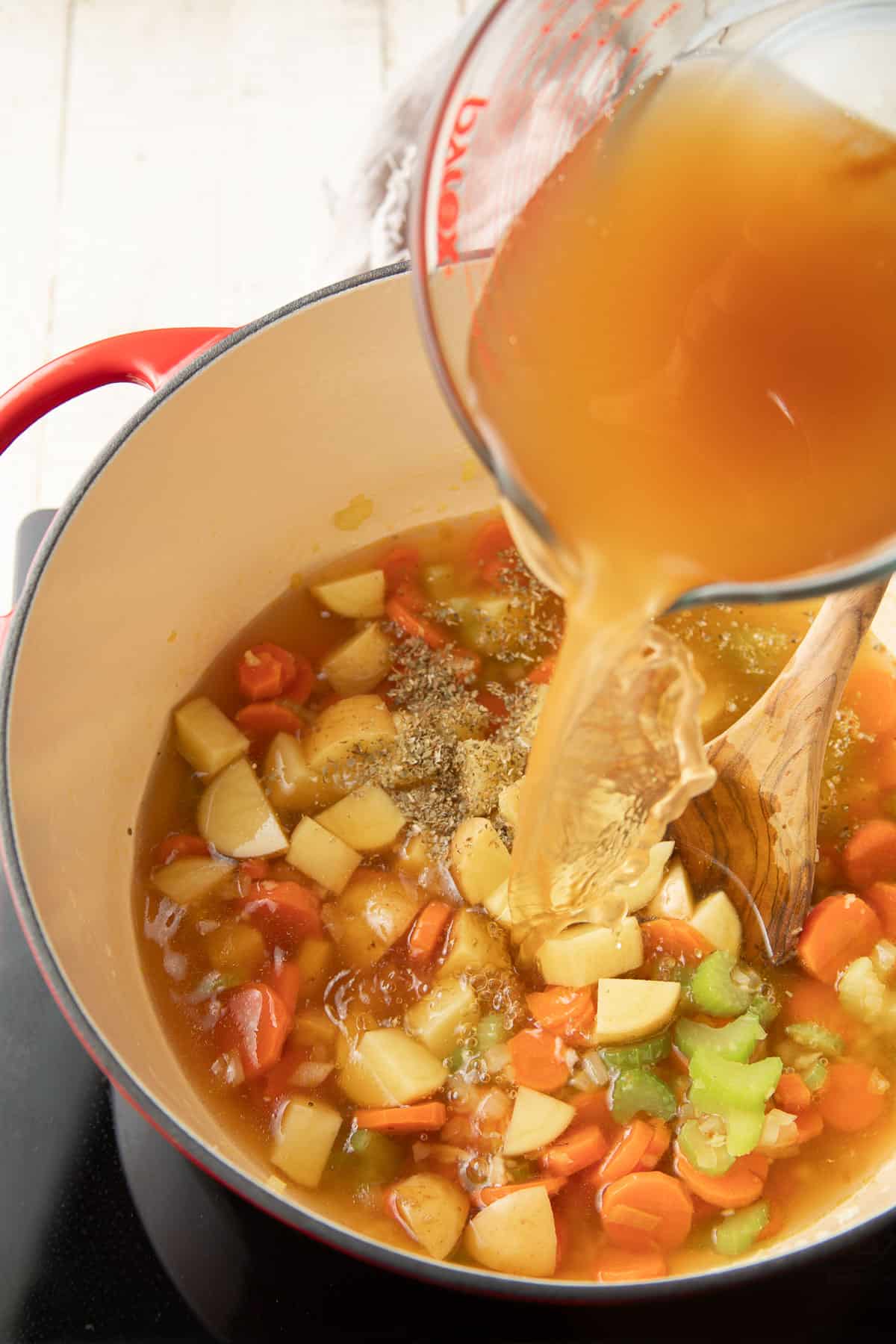 Broth being poured into a pot of vegetables.