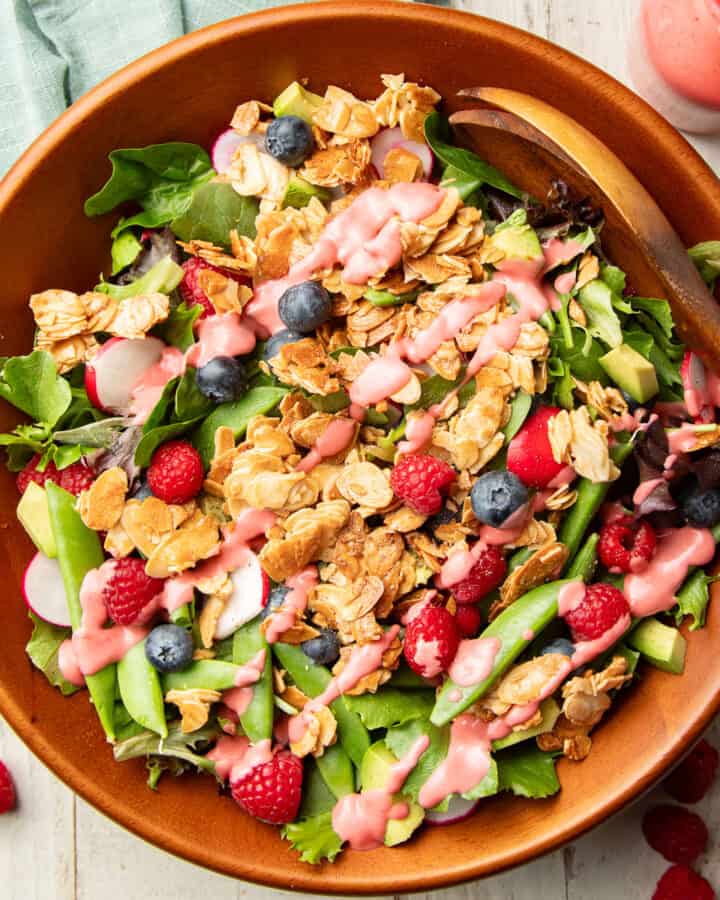 Salad with greens, almonds, berries and raspberry vinaigrette in a wooden bowl.