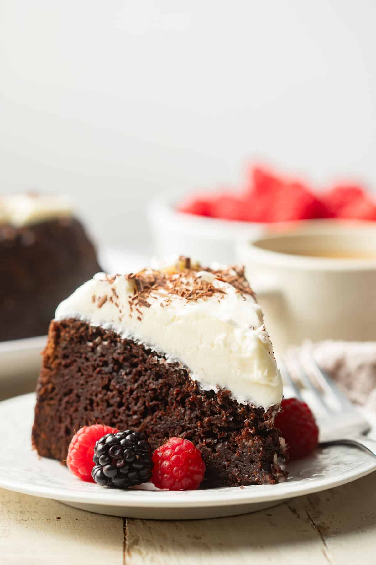 Slice of Vegan Guinness Cake on a dish with coffee cup and bowl of berries in the background.