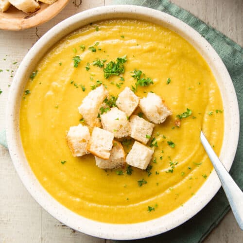 Bowl of Curried Parsnip Soup with parsley and croutons on top.
