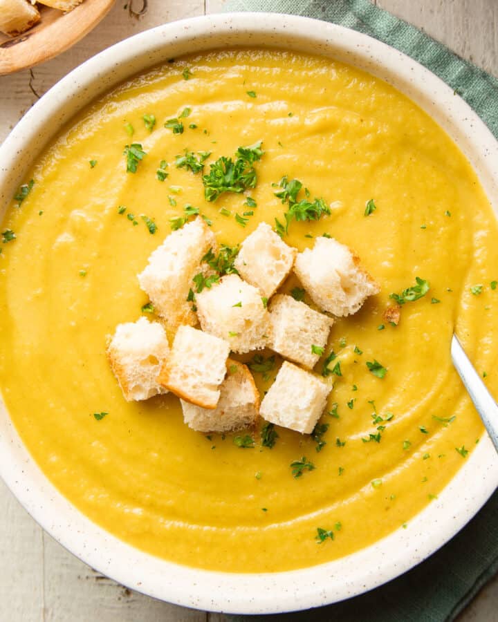 Bowl of Curried Parsnip Soup with parsley and croutons on top.