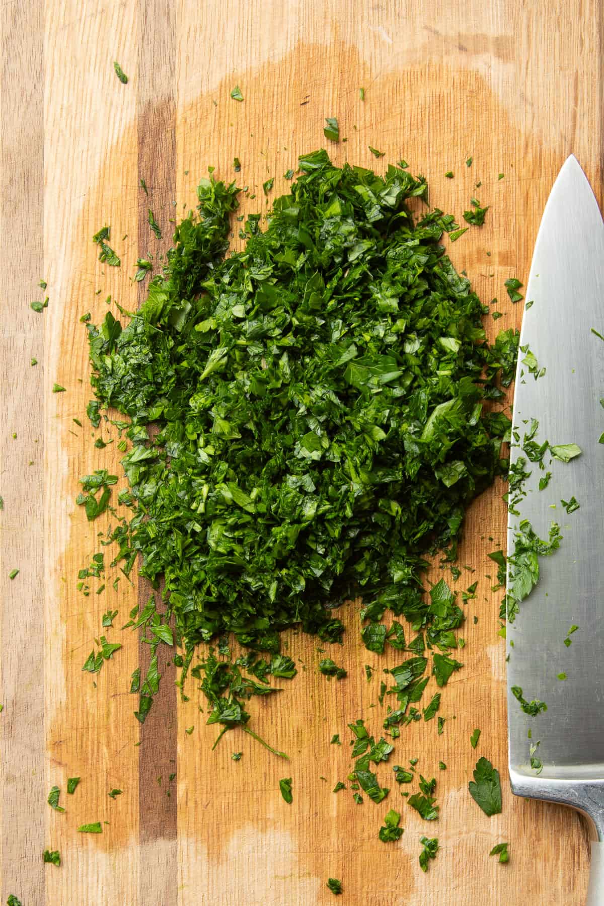 Finely chopped parsley on a cutting board with knife.