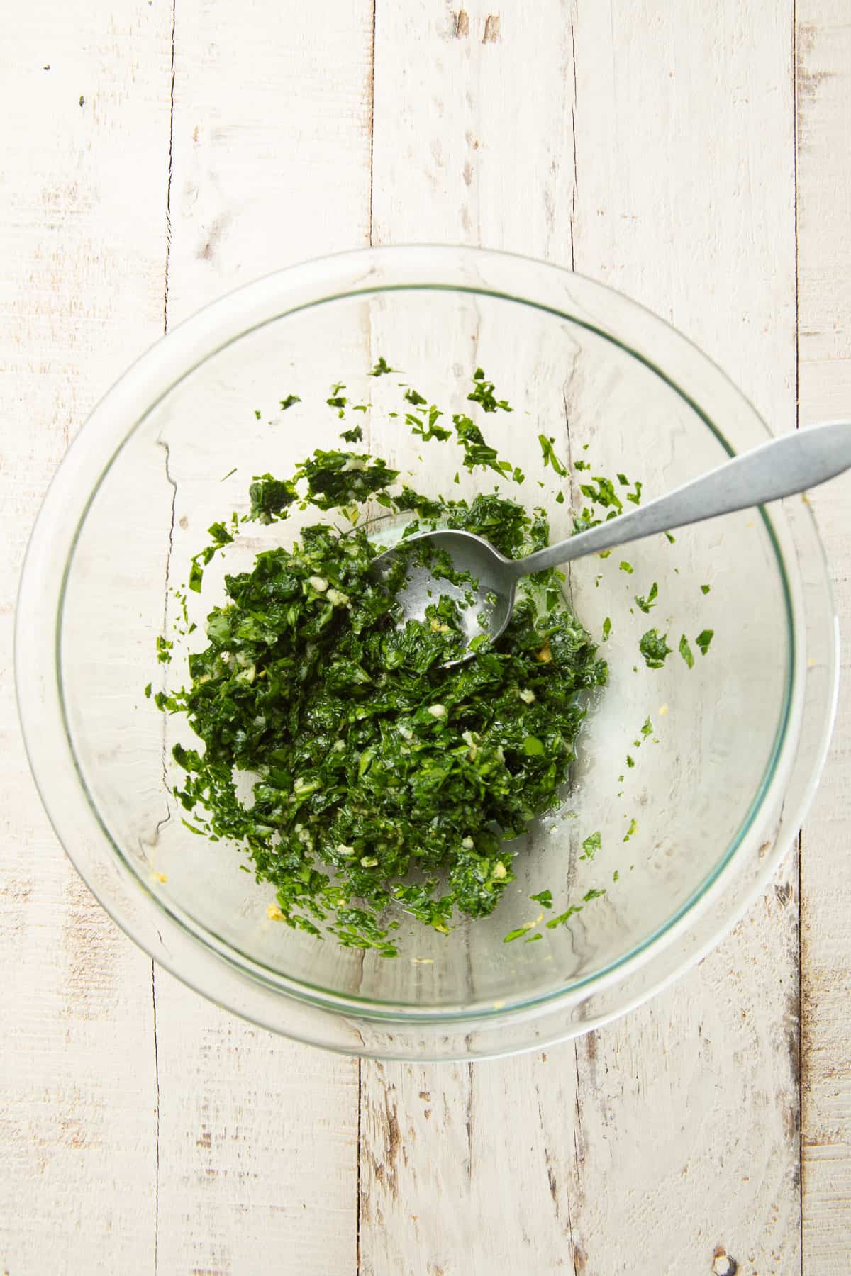 Gremolata sauce in a glass bowl with a spoon.