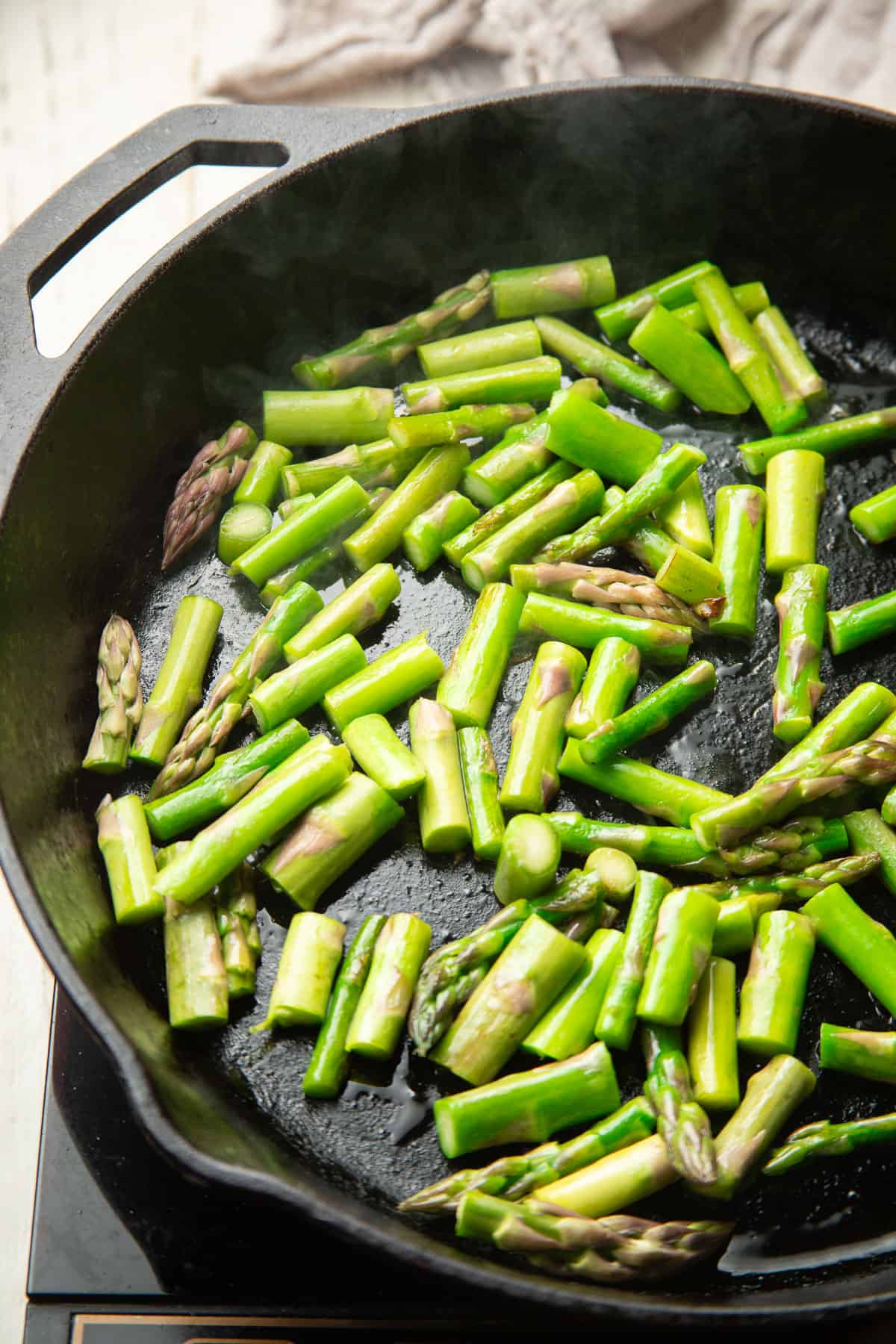Chopped asparagus spears cooking in a skillet.