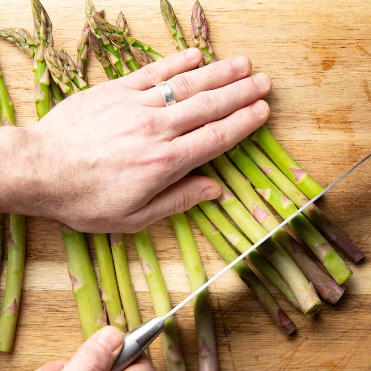 Hand using a knife to trim asparagus spears on a cutting board.