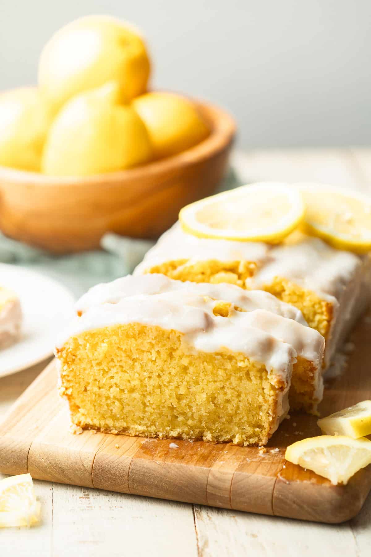 Vegan Lemon Loaf on a cutting board with bowl of lemons in the background.